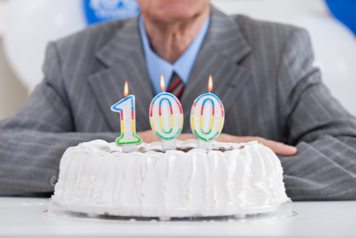 A man sitting behind a cake with “100” birthday candles.