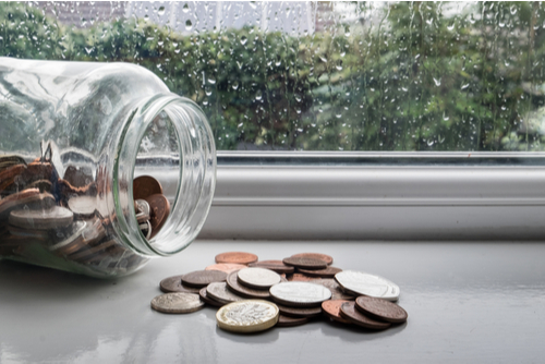 A jar of money tipped over with a rainy day in the background