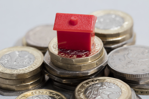 Plastic red house sitting on a pile of money