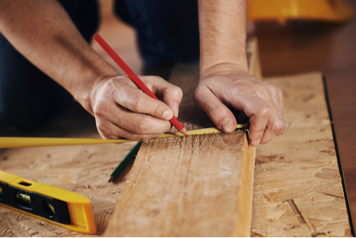 A workman measuring a wooden plank